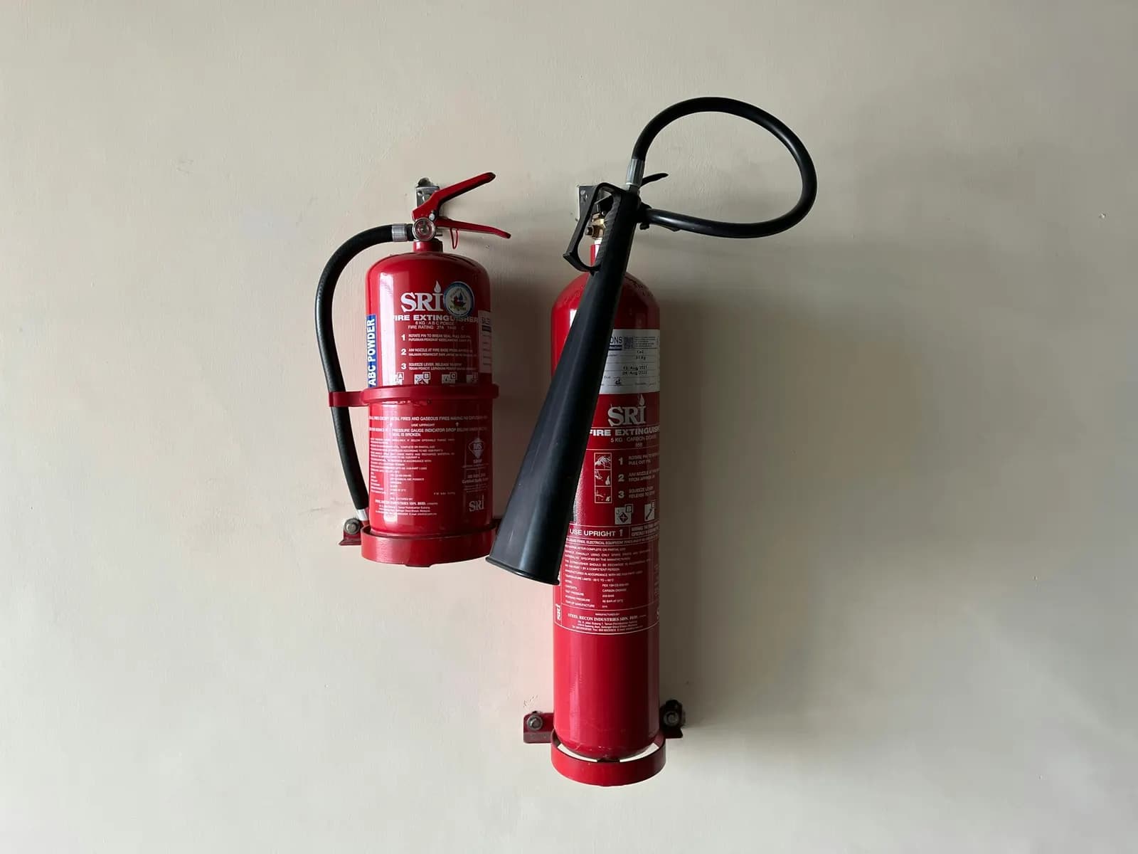 Estintore a polvere ABC ed estintore a CO₂ con cono nero, appesi affiancati a una parete